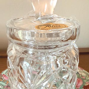Könnte beinhalten: Ein klarer Kristallbehälter mit Deckel und dekorativem Knauf. Der Behälter hat ein rautenförmiges Muster und ein goldenes Etikett mit der Aufschrift "Julio Crystals Made in Italy."