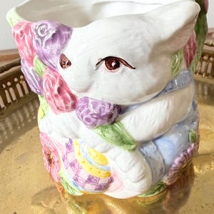 May include: A white ceramic mug with a black handle and the text "But First, Coffee" in a bold, black font. The mug is set against a blurred background, suggesting a cozy setting.