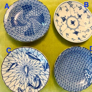 Puede incluir: Cuatro platos redondos de cerámica etiquetados A, B, C y D. El plato A tiene un patrón geométrico azul y blanco. El plato B presenta un diseño floral azul sobre blanco. El plato C muestra peces azules sobre una red. El plato D tiene un patrón de celosía azul.