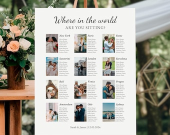 May include: A wedding seating plan displayed on an easel. The white sign has the text "Where in the world are you sitting?" with city names and guest lists. The bottom of the sign reads "Sarah & James | 12.03.2024".