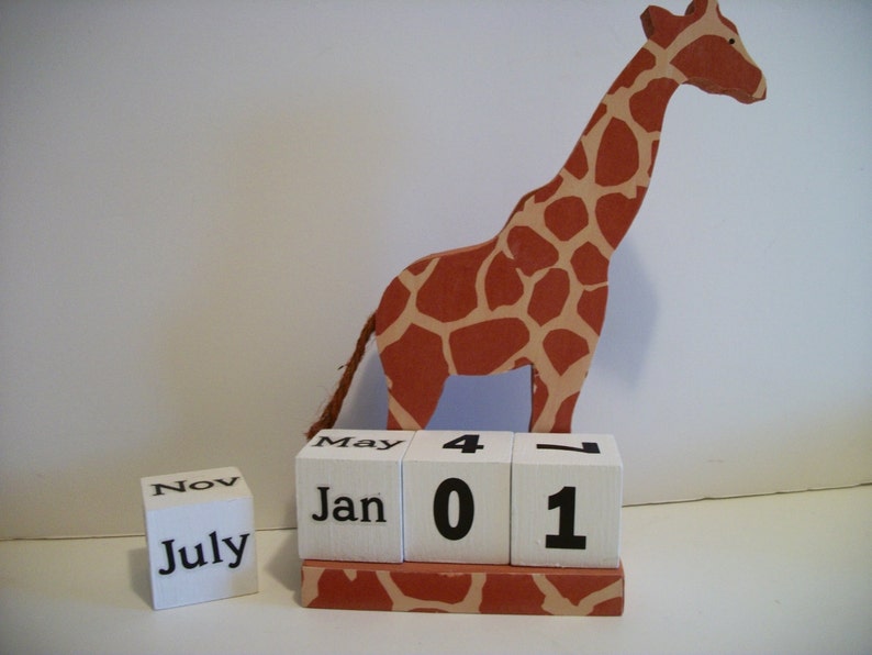 May include: A wooden giraffe figurine with brown and tan spots stands on a white block calendar with the months of January, May, July, and November displayed. The calendar also shows the date as 4-01.