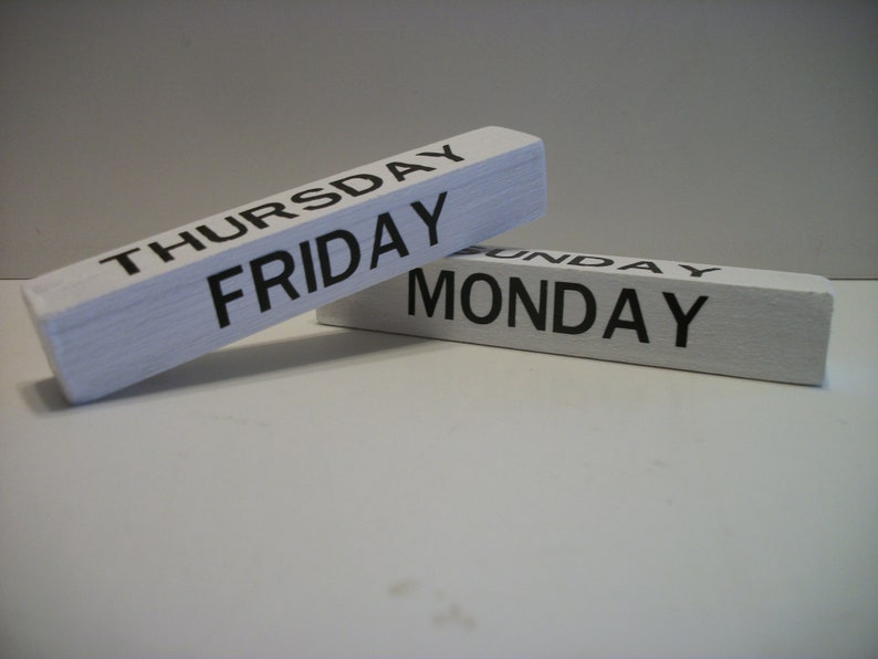 May include: Two white wooden blocks with black lettering. The top block reads "THURSDAY FRIDAY" and the bottom block reads "SUNDAY MONDAY".