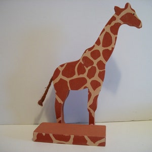 May include: A wooden giraffe figurine with a brown and tan spotted pattern. The giraffe is standing on a base with the same spotted pattern.