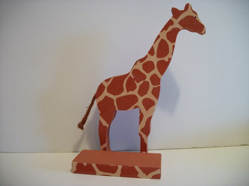 May include: A wooden giraffe figurine with a brown and tan spotted pattern. The giraffe is standing on a base with the same spotted pattern.