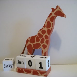 May include: A wooden giraffe figurine with a brown and orange spotted pattern stands on a white calendar block with the numbers 01 and 2. The calendar also has the months July, Jan, May and Nov.