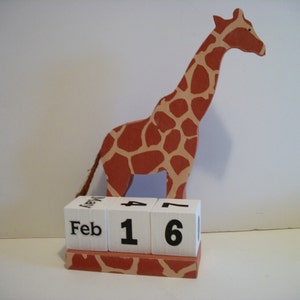 May include: A wooden giraffe figurine with a brown and orange spotted pattern, holding a block calendar that reads "Feb 16".