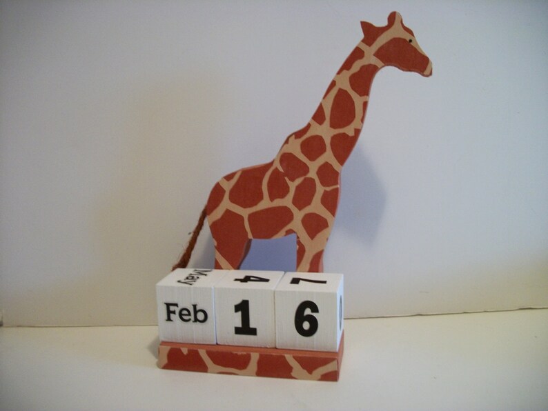 May include: A wooden giraffe figurine with a brown and orange spotted pattern, holding a block calendar that reads "Feb 16".