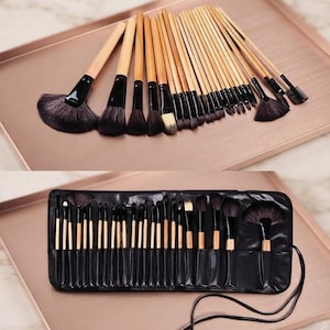 Può includere: Un set di pennelli per il trucco con manici in legno chiaro e setole nere, caratterizzato da varie forme tra cui pennelli a ventaglio, da cipria e di precisione. La collezione è mostrata sia aperta a ventaglio che in un astuccio nero.