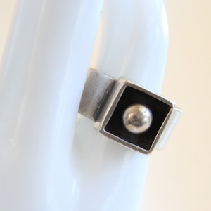May include: A silver ring with a square black bezel set with a silver sphere.