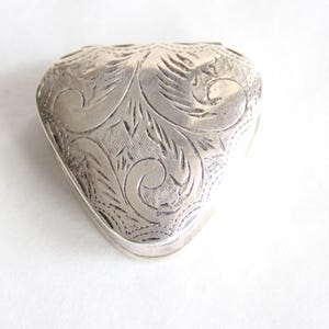 May include: A silver heart-shaped trinket box with an intricate floral design.