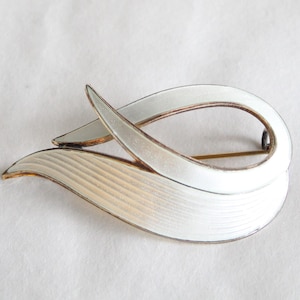 Peut inclure: Broche vintage avec un design en émail blanc. La broche présente une forme abstraite et fluide avec une épingle en métal doré. Le design comprend une boucle incurvée et un élément texturé en forme de feuille.