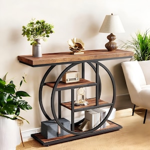 May include: A modern console table with a dark wood top and shelves, supported by a black metal frame. The table features a circular design with multiple shelves, and is decorated with a lamp, vase, and decorative objects. The table is 60 inches long.
