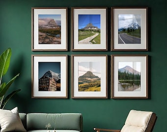 May include: A gallery wall set of six vertical rectangular framed prints featuring various mountain landscapes, including snowy peaks, a wooden boardwalk, a winding road, a large building, and a lake, all displayed in dark wood frames with white mats.