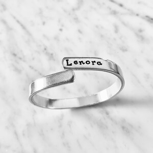 May include: A silver bangle bracelet with the name "Lenora" engraved on it.