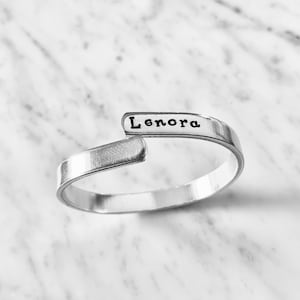 May include: A silver bangle bracelet with the name "Lenora" engraved on it.