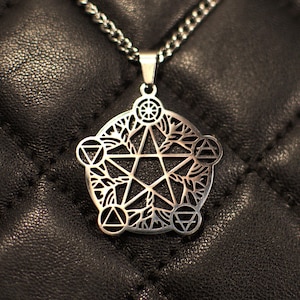 May include: Silver pendant necklace with a cut-out pentagram design, featuring leaf and geometric patterns. The pendant hangs from a matching chain. The necklace is set against a dark, textured backdrop.