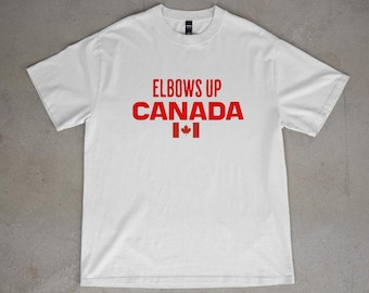 May include: White t-shirt with red text that says "Elbows Up Canada" and a small Canadian flag.