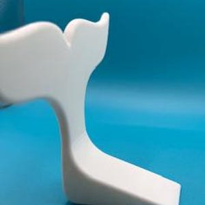 May include: A white, whale tail-shaped decorative object. The tail curves upwards, with a smooth, curved design. The object is set against a solid blue background, highlighting its form and shape. The object is made of a solid material.