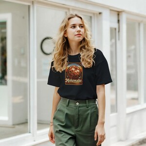 May include: Black t-shirt featuring a retro-style graphic of a planet with the text "Makemake". The graphic has a brown planet with orange, yellow, and blue stripes. The shirt is paired with green pants.