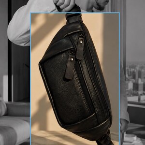 May include: A black leather belt bag featuring a textured surface, a main zippered compartment, and a smaller front zippered pocket. The bag includes matching black leather zipper pulls with metallic studs and an adjustable strap for carrying.