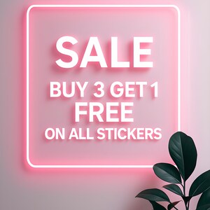 May include: A pink neon sign with the word "SALE" in white, along with "BUY 3 GET 1 FREE ON ALL STICKERS." A dark green plant is in the lower right corner. The sign has a square shape with rounded corners.