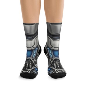 May include: A pair of crew socks featuring a detailed graphic print of metallic robotic armor. The design includes silver plating, intricate mechanical components, dark grey structural elements, and glowing blue light accents throughout the pattern.
