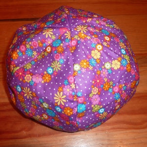 May include: A purple fabric hat with a floral pattern in various colors, including pink, orange, yellow, and blue. The hat has a polka dot design and is likely handmade.