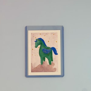 May include: A small rectangular trading card featuring a watercolour painting of a green winged horse with a blue mane and tail. The horse stands on a pinkish-brown cloud against a light background filled with small yellow star shapes.