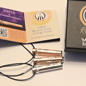 May include: An image featuring an energy tuner set, with three metallic cylinders on black cords, a brochure, and a black box. The box and brochure display the text "Rise & Thrive" and "528 Hz 'Miracle Tone' Energy Tuner".