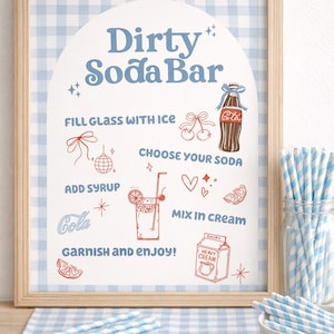 May include: A framed sign with a light blue and white gingham background. The sign reads "Dirty Soda Bar" with instructions and illustrations for making a soda. Blue and white striped straws and a bowl are in the foreground.