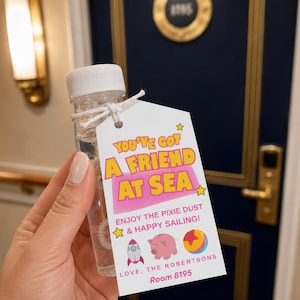 May include: A clear plastic bottle filled with liquid, featuring a white cap and a white rectangular tag tied with string. The tag displays the text YOU'VE GOT A FRIEND AT SEA, ENJOY THE PIXIE DUST & HAPPY SAILING, LOVE, THE ROBERTSONS, Room 8195.
