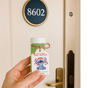 Puede incluir: Una pequeña botella verde con tapa blanca y una etiqueta con un personaje de dibujos animados Stitch con gorro de Papá Noel. La etiqueta dice "You've Been Pixie Dusted". La botella está atada con hilo.