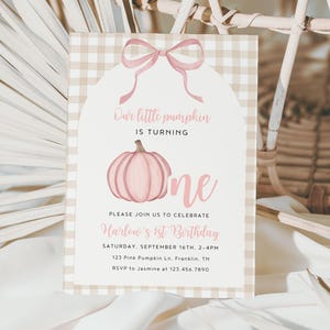 May include: A light pink and tan gingham patterned invitation card with a pink bow and pumpkin illustration. The text reads "Our little pumpkin is turning one." Additional text includes the event details: date, time, location, and RSVP information.