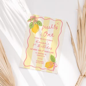 May include: A birthday invitation with a yellow and white striped background and a pink wavy border. The text "freshly One" is at the top, with details about the birthday party below, including the date, time, and location. Lemon illustrations are featured.