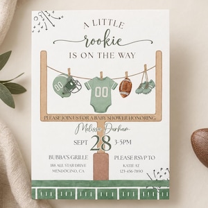 Könnte beinhalten: Eine weiße Babyparty-Einladungskarte mit einer Football-Torstangen-Grafik und einer Wäscheleine, an der ein Helm, ein grüner Body, ein Football und Stollen hängen. Der Text lautet A LITTLE rookie IS ON THE WAY, PLEASE JOIN US FOR A BABY SHOWER HONORING.