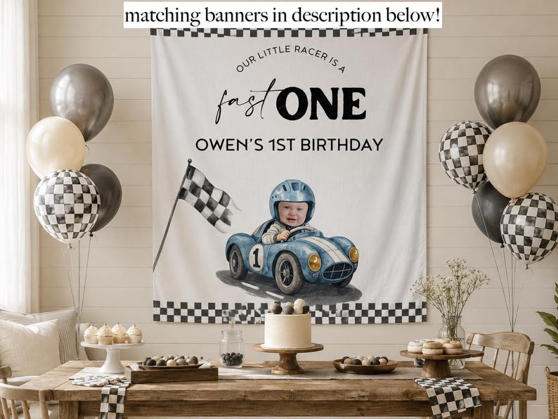 May include: A white fabric banner featuring a black checkered border, the text "OUR LITTLE RACER IS A fast ONE" and "OWEN'S 1ST BIRTHDAY", and a watercolor illustration of a child in a blue race car with a checkered flag.