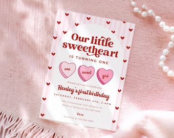 May include: A pink and white invitation card with a heart theme. The text reads "Our little sweetheart is turning one." The card includes the name "Henley" and event details. Red hearts and a pearl necklace are also visible.