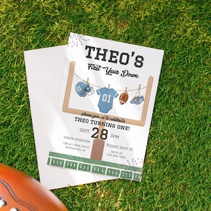 Könnte beinhalten: Eine weiße Einladungskarte mit dem Text "THEO'S First Year Down" und Illustrationen zum Thema American Football. Die Einladung enthält Details für eine Feier zum ersten Geburtstag, mit einem Football und einem Footballfeld-Design. Die Karte befindet sich auf einem grünen Gras-Hintergrund.