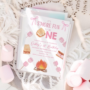 May include: A stack of invitation cards with a pink and white s'mores theme. The text reads "It's S'more Fun to be One" and invites guests to Oakley's 1st Birthday. Watercolor illustrations of marshmallows, a campfire, and s'mores are featured.