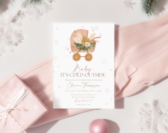 May include: A baby shower invitation with a winter theme. The card features a decorative baby carriage illustration with floral accents. The text reads "Baby, It's Cold Outside." The invitation is surrounded by a pink sweater, a wrapped gift, and decorative snowflakes.