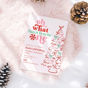 May include: A pink and white birthday invitation with the text "Oh what fun it is to be one." The invitation features a candy cane and a Christmas tree design with bows. The invitation includes the event details: Emilia's first birthday, Saturday, December 8, 2-4 PM.