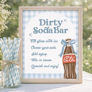 May include: A framed sign with a light blue gingham background and the words "Dirty Soda Bar." It includes instructions for making a soda, and a cartoon illustration of a cola bottle with a blue bow. A jar of blue and white striped straws sits to the left.