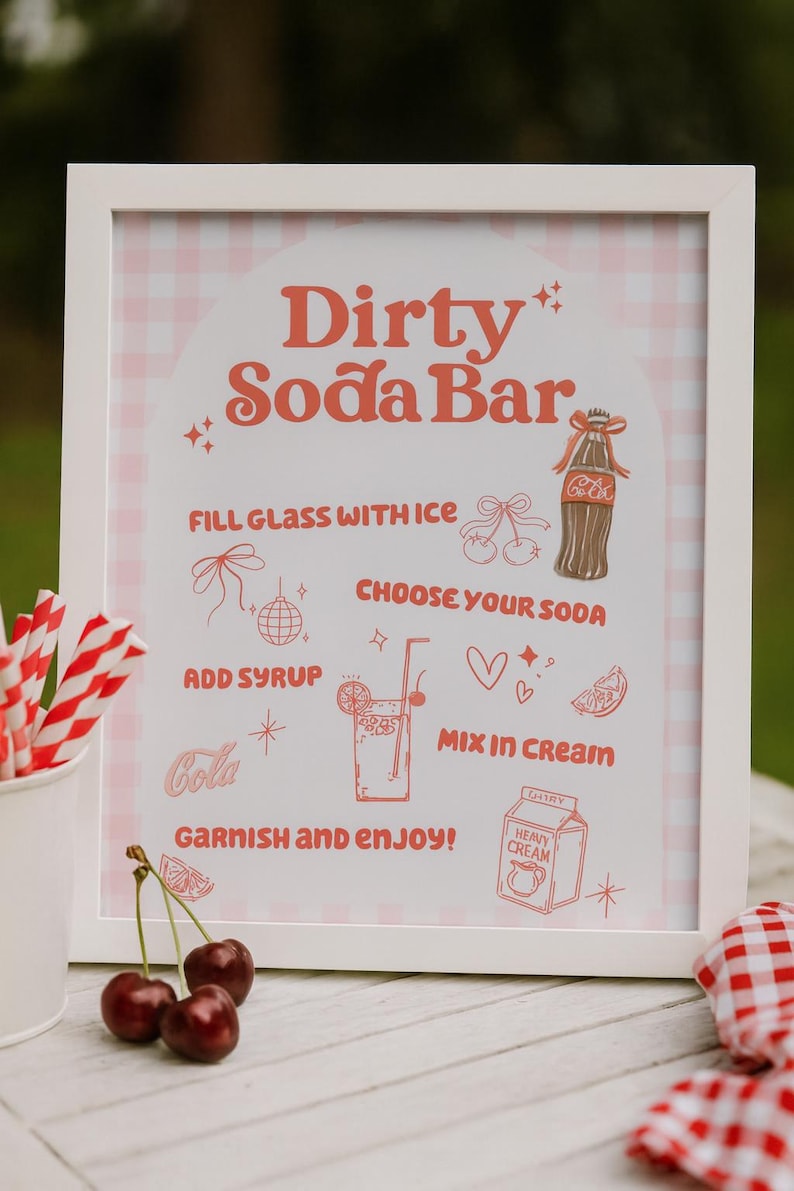 May include: A framed sign with the text "Dirty Soda Bar" in a retro font. The sign includes instructions and illustrations for making a soda, with a pink and white gingham background. Red and white striped straws and cherries are in the foreground.