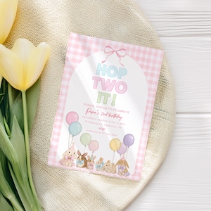Puede incluir: Una invitación de cumpleaños con el texto "Hop Two It!" en colores pastel, con ilustraciones de conejitos sosteniendo globos. La invitación está sobre un fondo rosa de cuadros, con detalles para el 2º cumpleaños de Piper.
