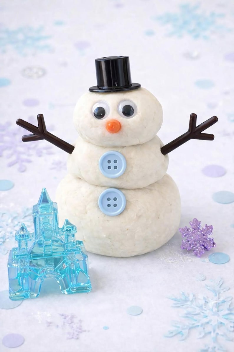 Pu&ograve; includere: Un pupazzo di neve stravagante fatto di pasta, con un cappello a cilindro nero, occhi finti e un naso arancione. Braccia di ramoscelli marroni e dettagli di bottoni blu completano il design. Sono presenti anche un castello blu e un fiocco di neve viola.