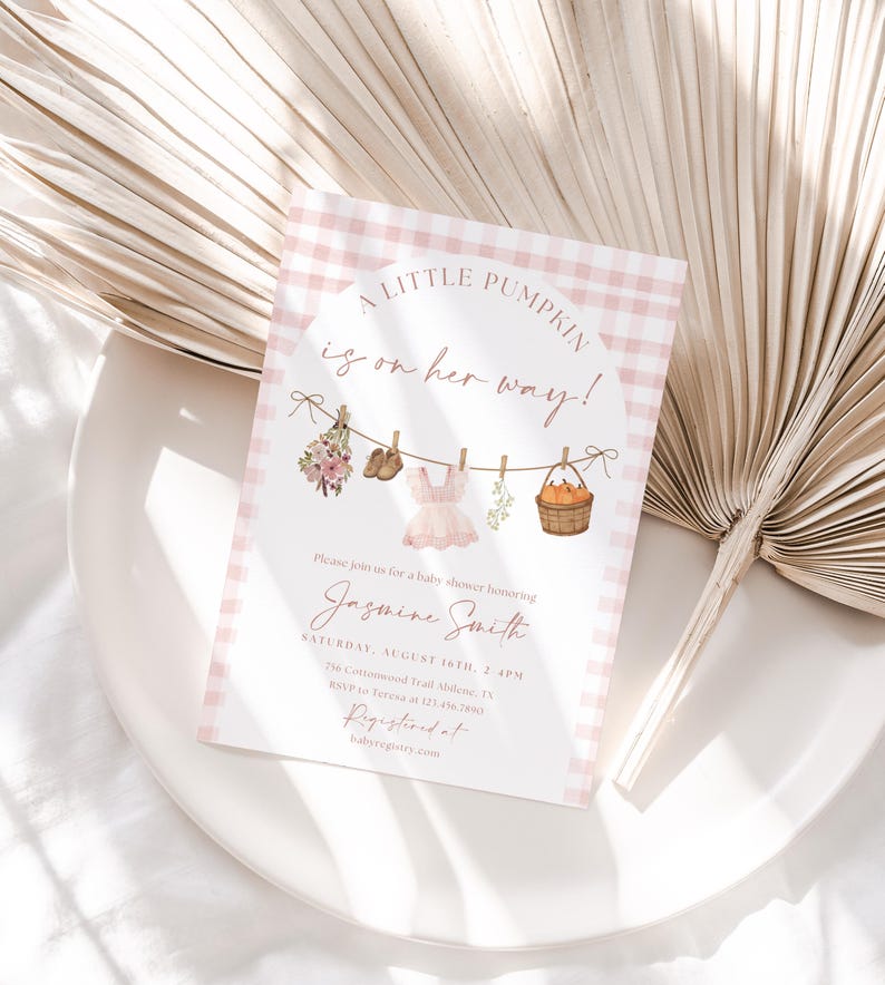 Peut inclure: Une invitation &agrave; une baby shower avec une bordure rose &agrave; carreaux et le texte "A Little Pumpkin is on her way!". L'invitation pr&eacute;sente des illustrations de v&ecirc;tements de b&eacute;b&eacute;, de fleurs et d'un panier de citrouilles. Le nom "Jasmine Smith" est &eacute;galement affich&eacute;.