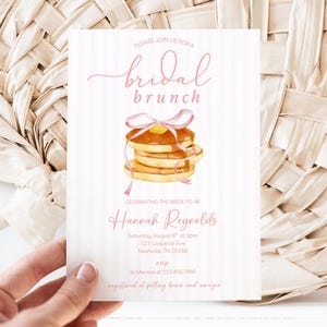 May include: A bridal brunch invitation featuring a watercolour illustration of pancakes with syrup and a pink ribbon. The invitation includes the text "Please join us for a bridal brunch" and the bride's name.
