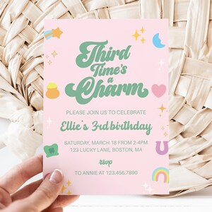 May include: A pink invitation card with the text "Third Time's a Charm" in green script, celebrating Ellie's 3rd birthday. The card includes details like the date, time, and location, along with a rainbow, heart, and other decorative elements.