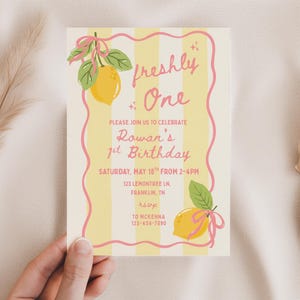 May include: A birthday invitation with a lemon theme. The card features yellow stripes, pink accents, and illustrations of lemons with green leaves. Text reads "freshly One" and details for Rowan's 1st birthday.