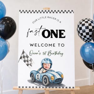 Puede incluir: Un letrero con el texto "Our Little Racer is a Fast One" da la bienvenida a los invitados al 1er cumpleaños de Owen. El letrero presenta una ilustración de un bebé en un coche de carreras azul, rodeado de globos.